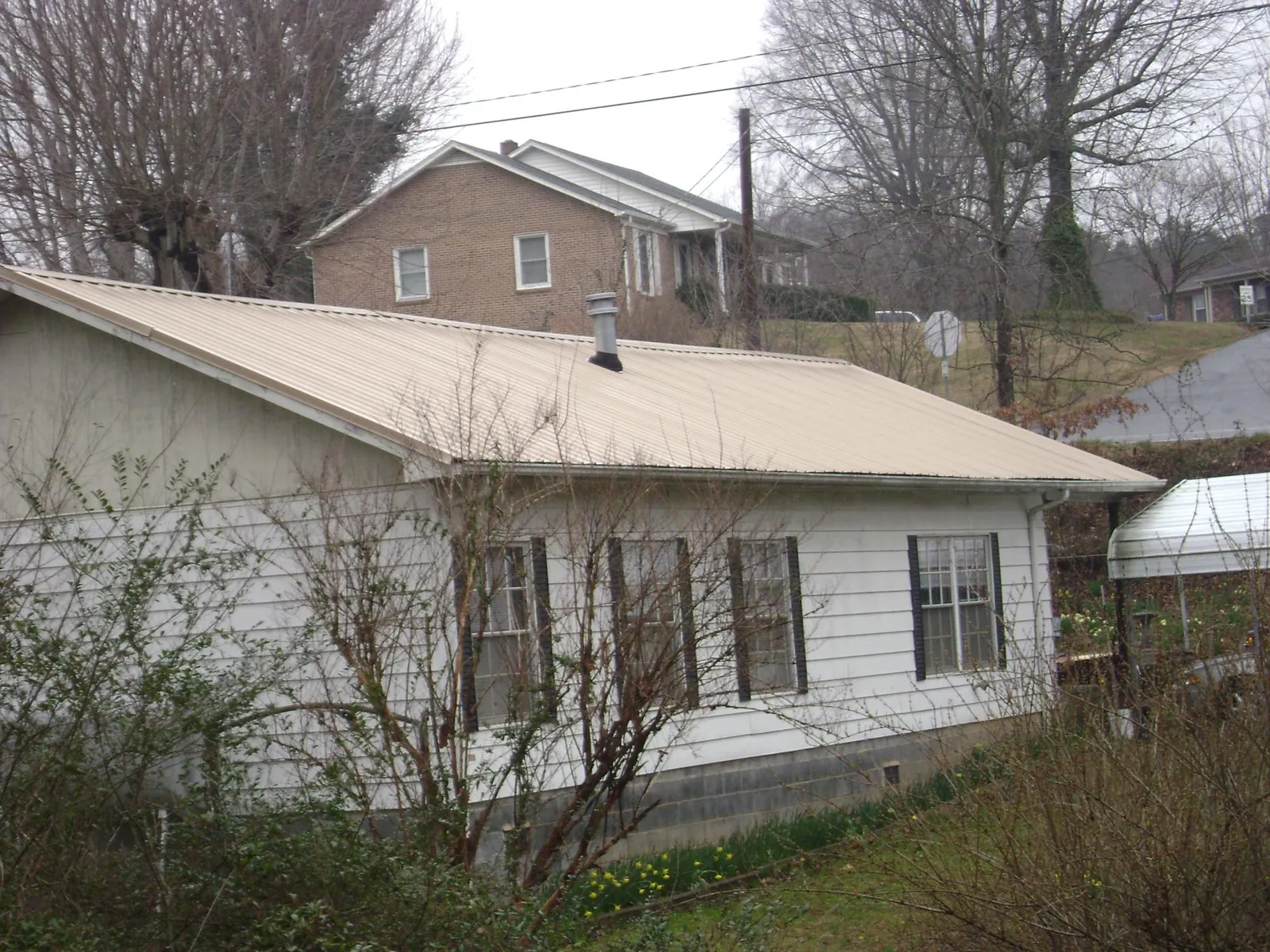 Tan metal roof on a white sided house set into a hillside — Commercial Roofing by Roofing Brothers in Brewster